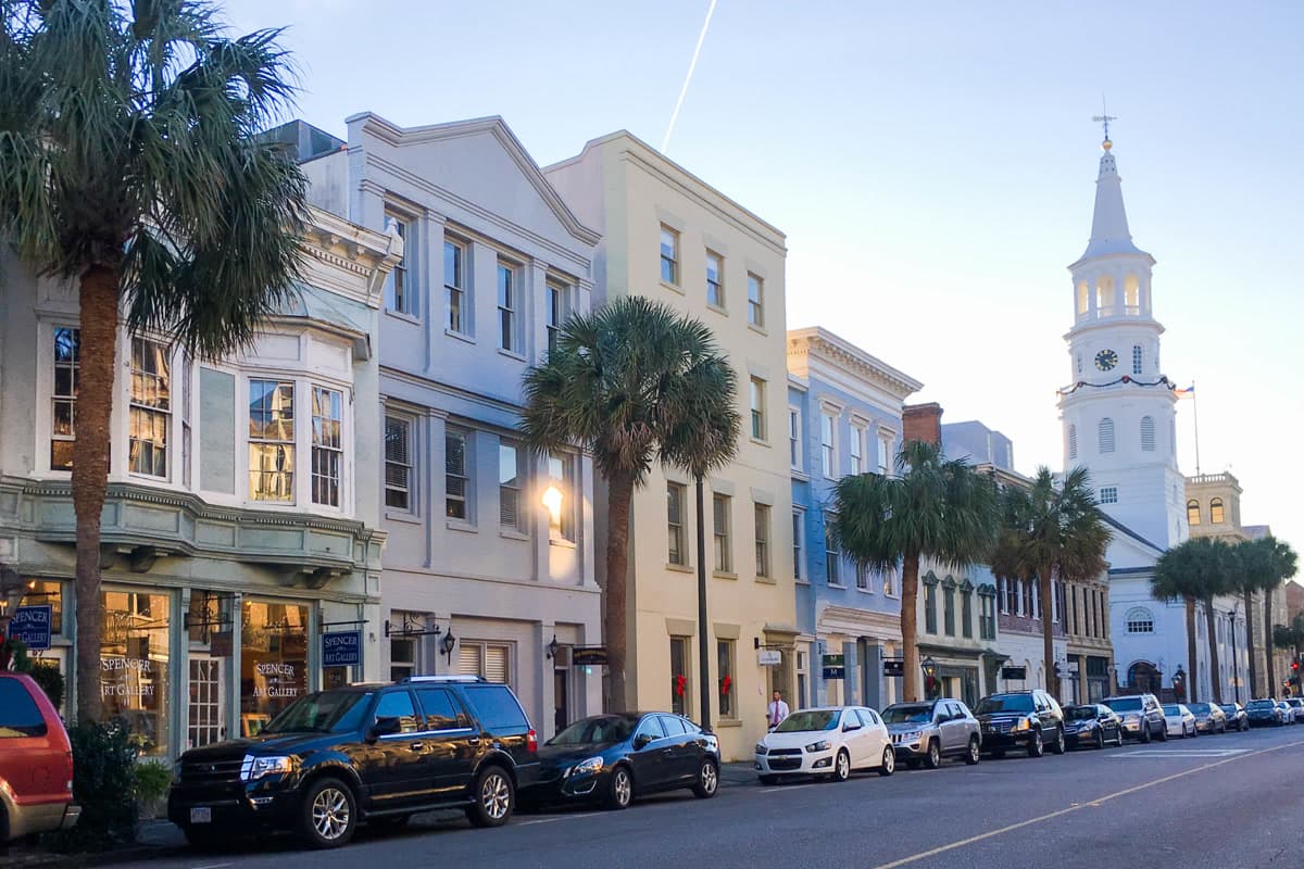Historic Charleston downtown street with pastel buildings, palm trees, and a church steeple